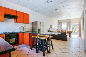 Cocina moderna con una isla central, taburetes de madera y una zona de comedor con sofá y cortinas.