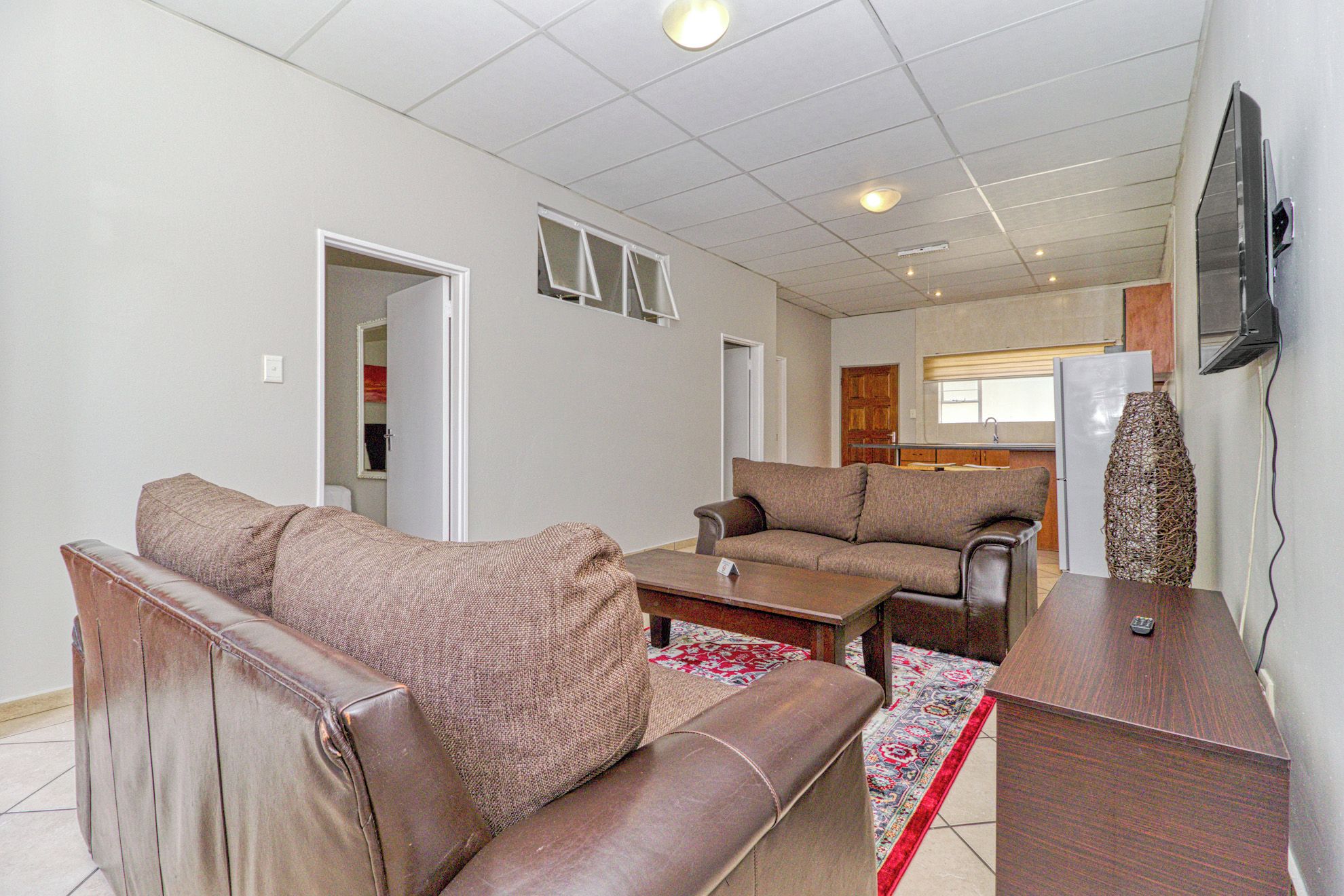 A living room with two sofas, a coffee table, a TV, and a kitchen in the background.