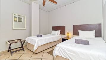 Een hotelkamer met twee bedden, een plafondventilator, een nachtkastje met lamp en een kleine houten trap.