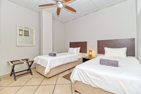Une chambre d’hôtel avec deux lits, un ventilateur de plafond, une table de chevet avec une lampe et une petite échelle en bois.