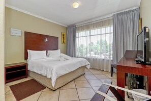 Ein Hotelzimmer mit einem Bett, einem Schreibtisch, einem Fernseher und einem fenster mit Vorhängen.