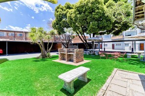A backyard with a barbecue area, a stone bench, and a covered seating area. - Bm Gardens Apartment Hotel (Germiston)