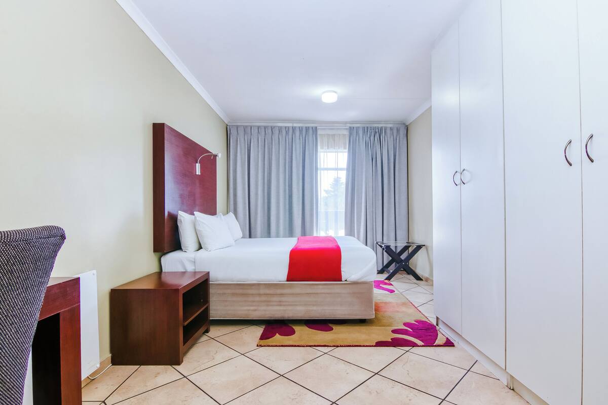 A bedroom with a bed, a desk, a wardrobe, and a window with curtains.