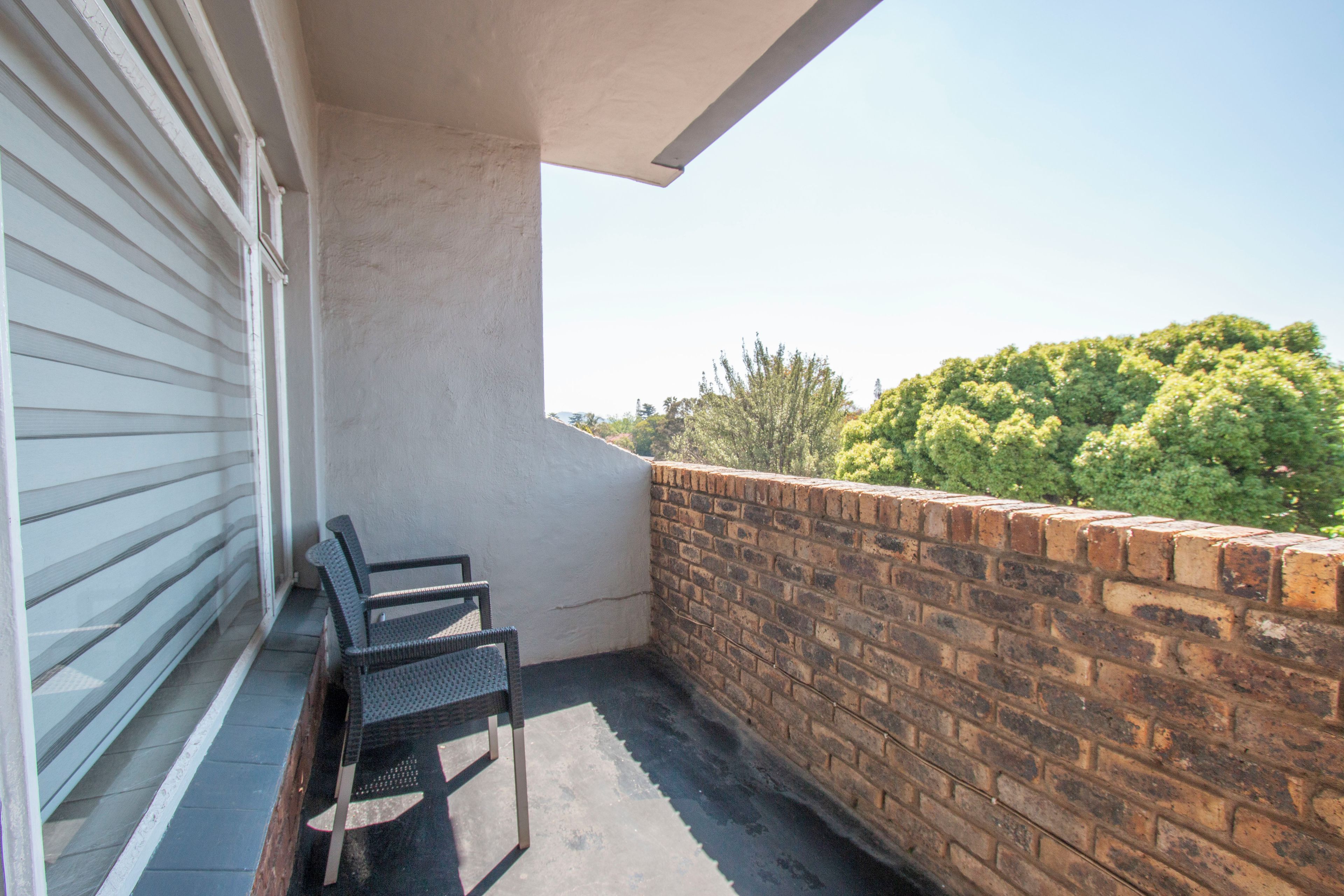 Een balkon met een bakstenen muur, een raam met zonwering en een stoel.