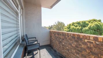 Een balkon met een bakstenen muur, een raam met zonwering en een stoel.