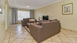 A living room with a sofa, a coffee table, a TV, and a framed picture on the wall. - Bm Gardens Apartment Hotel (Germiston)