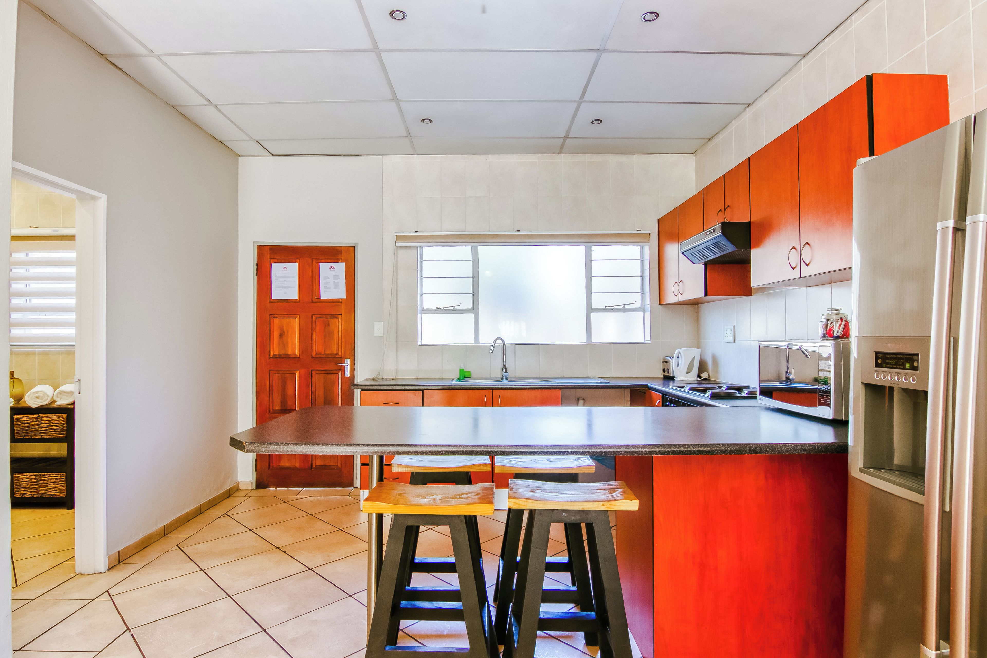 A kitchen with a central island, wooden stools, a refrigerator, and a window.