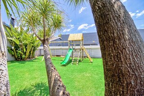A backyard with a wooden playset, including a slide and climbing area, surrounded by green grass and trees. - Bm Gardens Apartment Hotel (Germiston)
