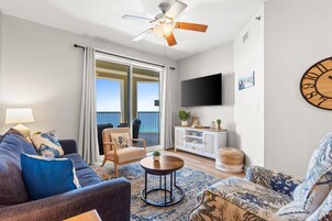 A living room with a sofa, armchair, and a coffee table. There is a television mounted on the wall and a ceiling fan.
