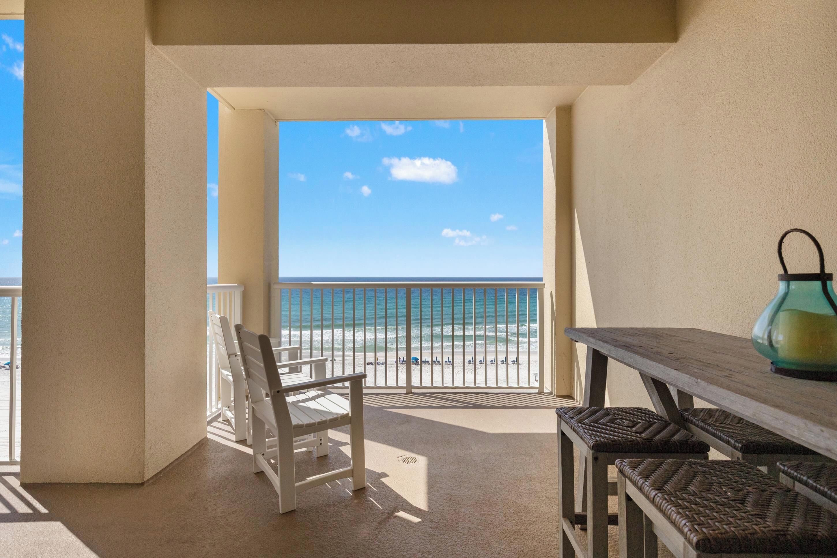 A balcony with a view of the beach, a table, and a chair.