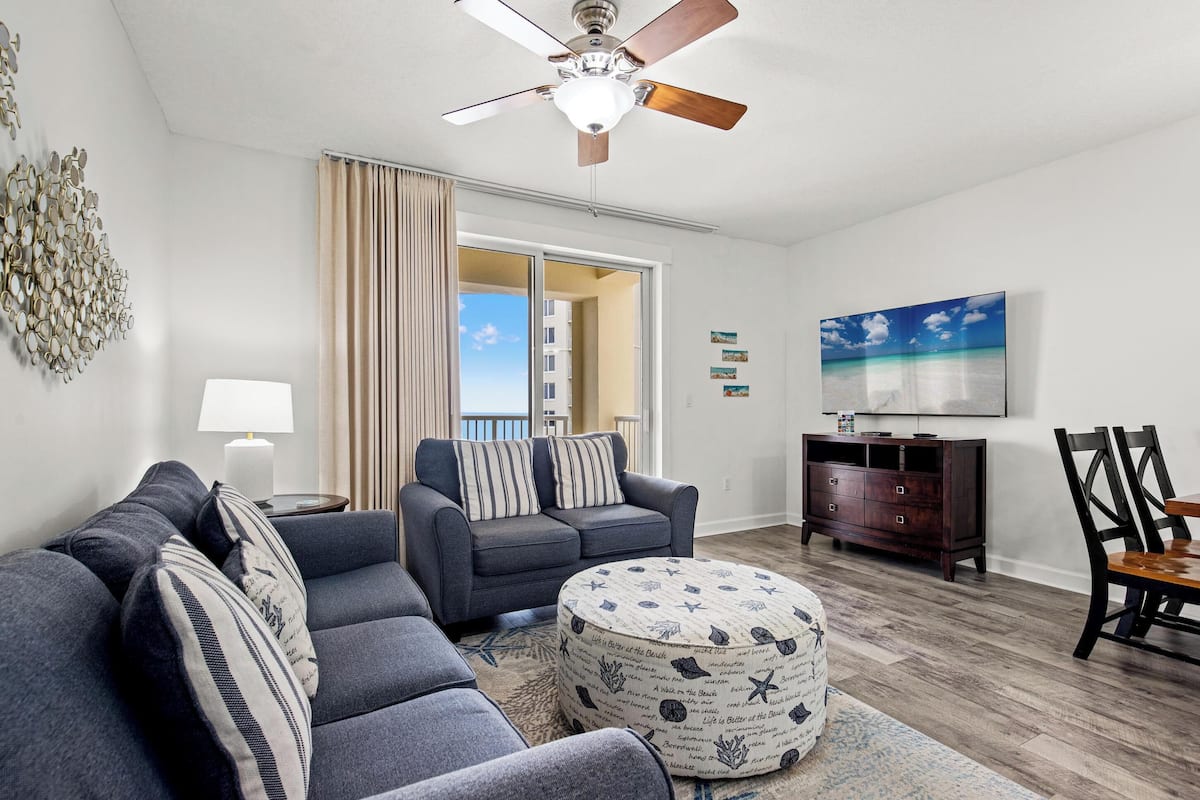 A living room with a gray sofa, a round ottoman, a wooden cabinet, and a ceiling fan.