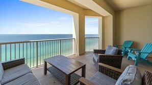 A balcony with wicker furniture, a wooden table, and turquoise Adirondack chairs overlooking the ocean. - Grand Panama Beach Resort by Panhandle Getaways (Panama City Beach)