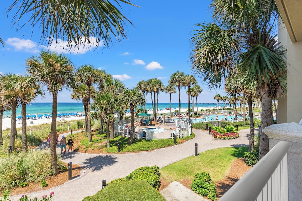 A resort with a pool, palm trees, and a beach view.