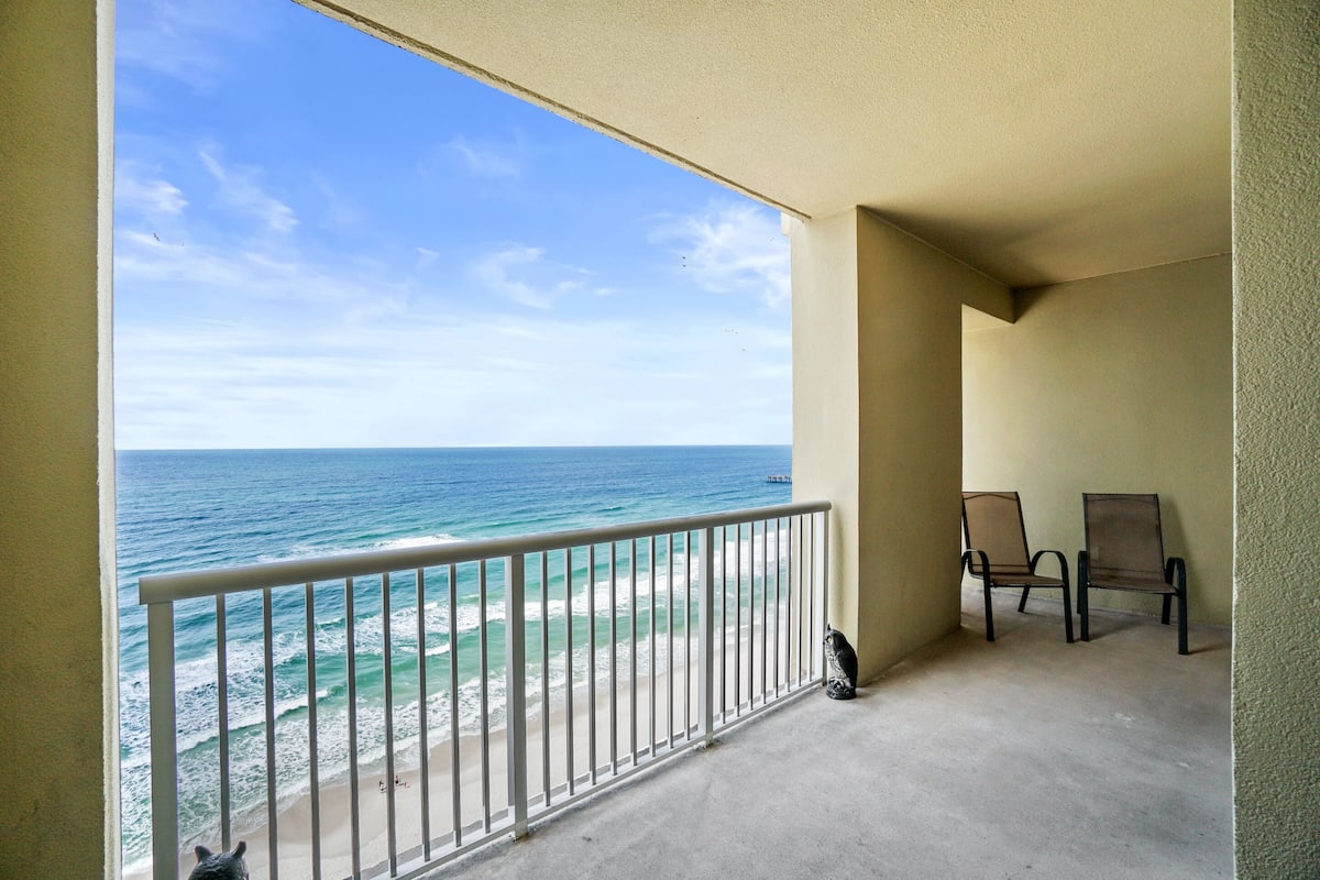 A balcony with a view of the ocean, two chairs, and a concrete floor.