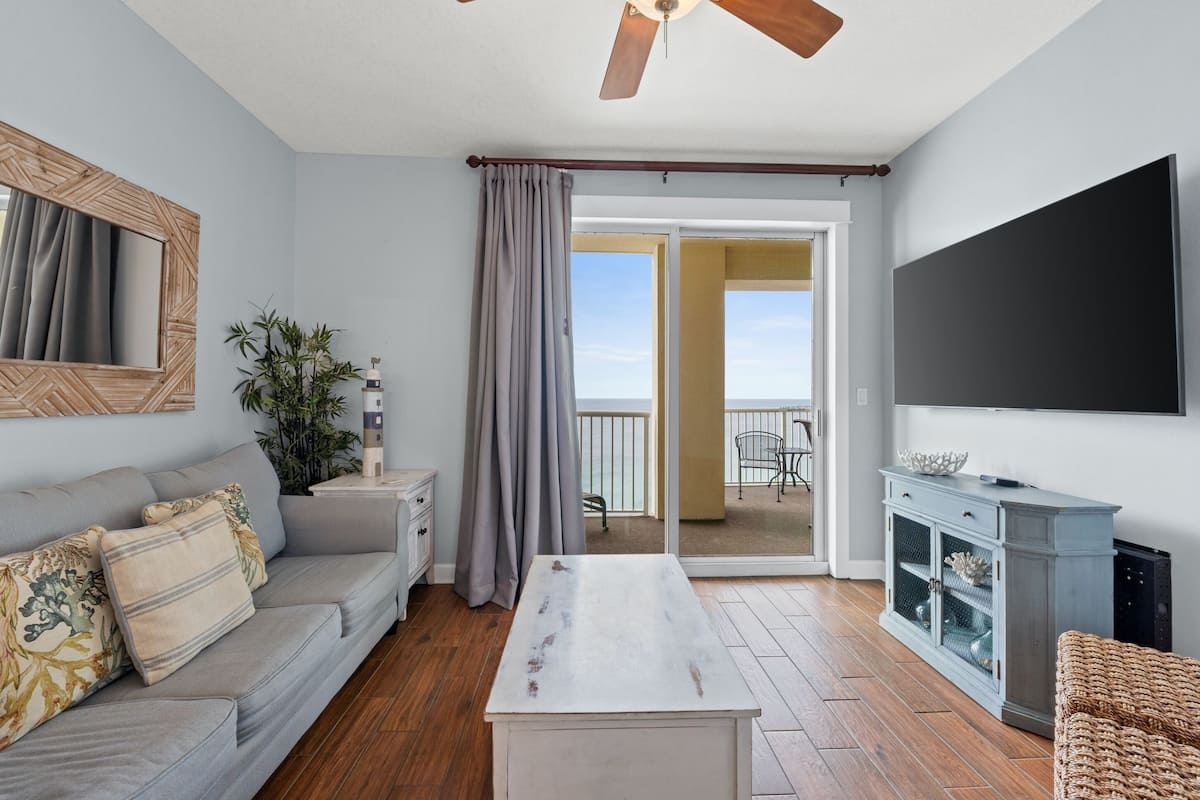 A living room with a sofa, a coffee table, a TV, and a sliding glass door leading to a balcony.