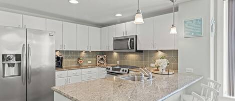 A modern kitchen with granite countertops, stainless steel appliances, and white cabinetry.