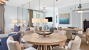 A modern living room with a round wooden table, comfortable seating, and a large mirror reflecting the space. - Grand Panama Beach Resort by Panhandle Getaways (Panama City Beach)