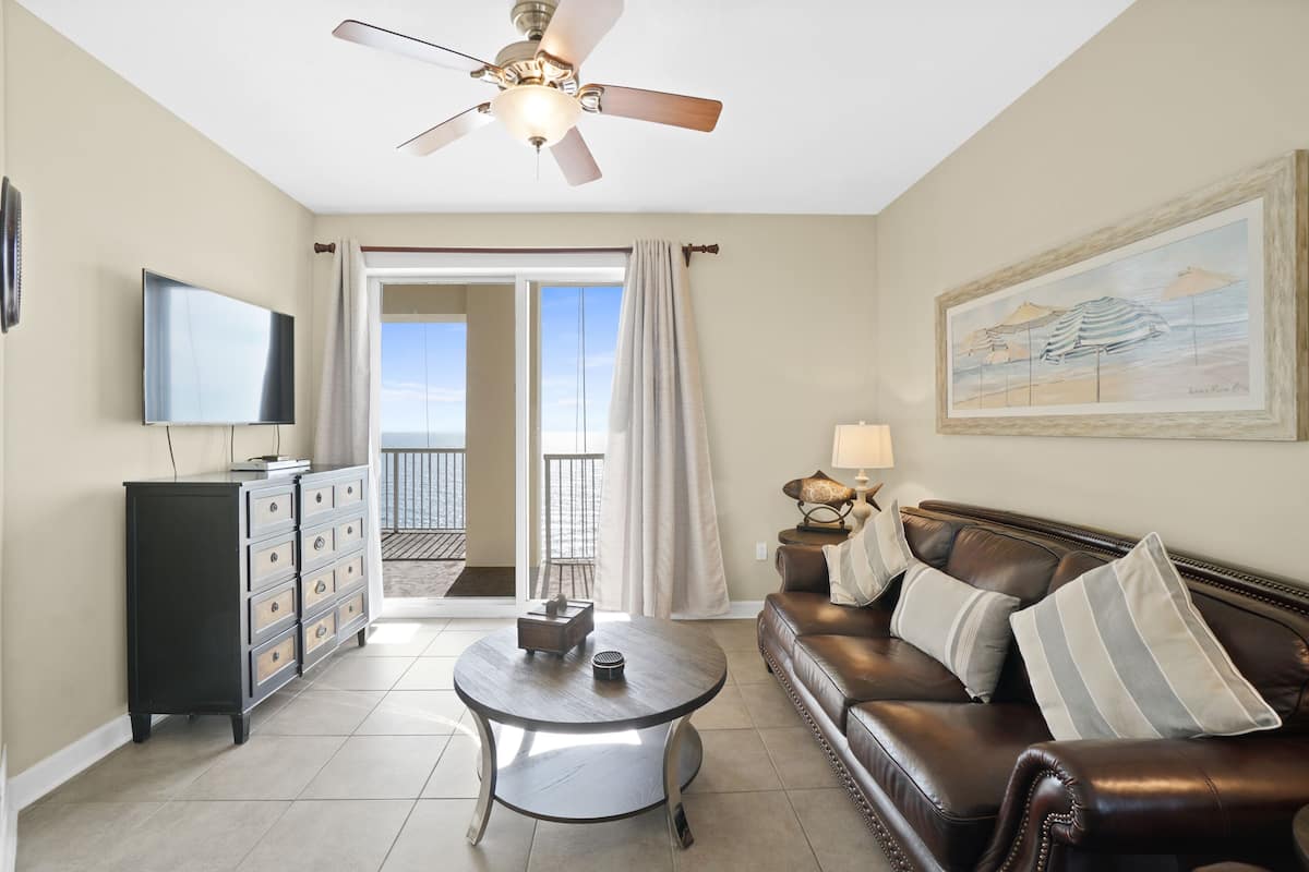 A living room with a ceiling fan, a television, a coffee table, a leather sofa, and a painting on the wall.