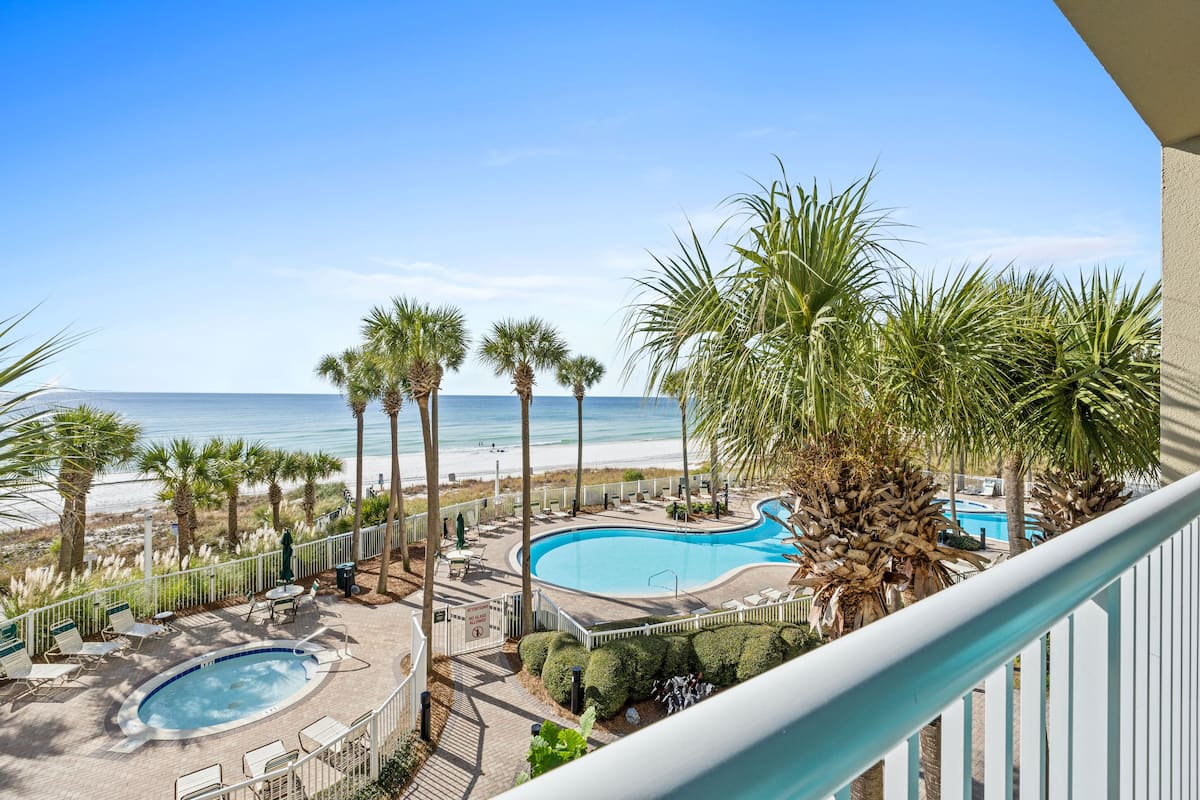 A pool area with a view of the beach, surrounded by palm trees and lounge chairs.
