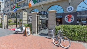 A hotel entrance with flags, a bike and scooter rental sign, and a sign for a restaurant. - Unit Number 318 Cape Royale Luxury Apartments (Cape Town)
