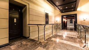A hotel lobby with a marble floor, a black door with a number plaque, a glass railing, and a staircase leading to another area. - Unit Number 318 Cape Royale Luxury Apartments (Cape Town)