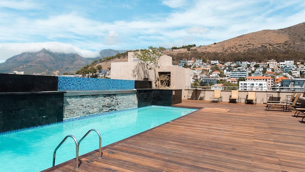 A rooftop pool with a wooden deck, a stone wall, and a view of a hillside town. - Unit Number 318 Cape Royale Luxury Apartments (Cape Town)