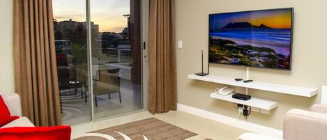 Un salón moderno con un ventanal corredero que da a un balcón, un televisor de pantalla plana en la pared y un sillón rojo.