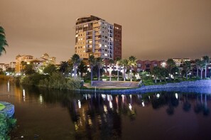 A waterfront hotel with a reflection pool, palm trees, and illuminated buildings. - Manhattan Luxury Apartments (Cape Town)