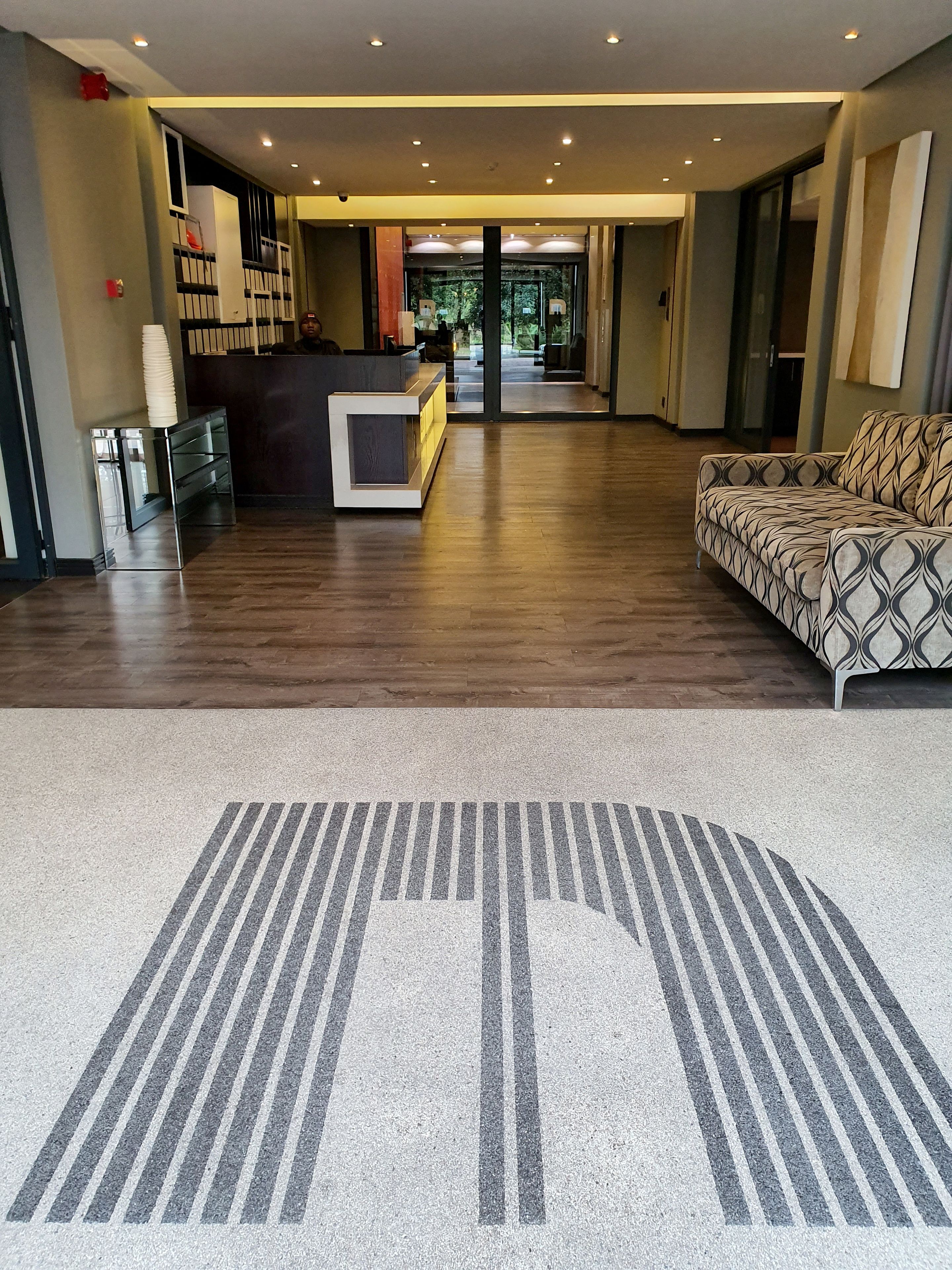 A spacious lobby with a reception desk, a patterned sofa, and a carpet with a large logo.