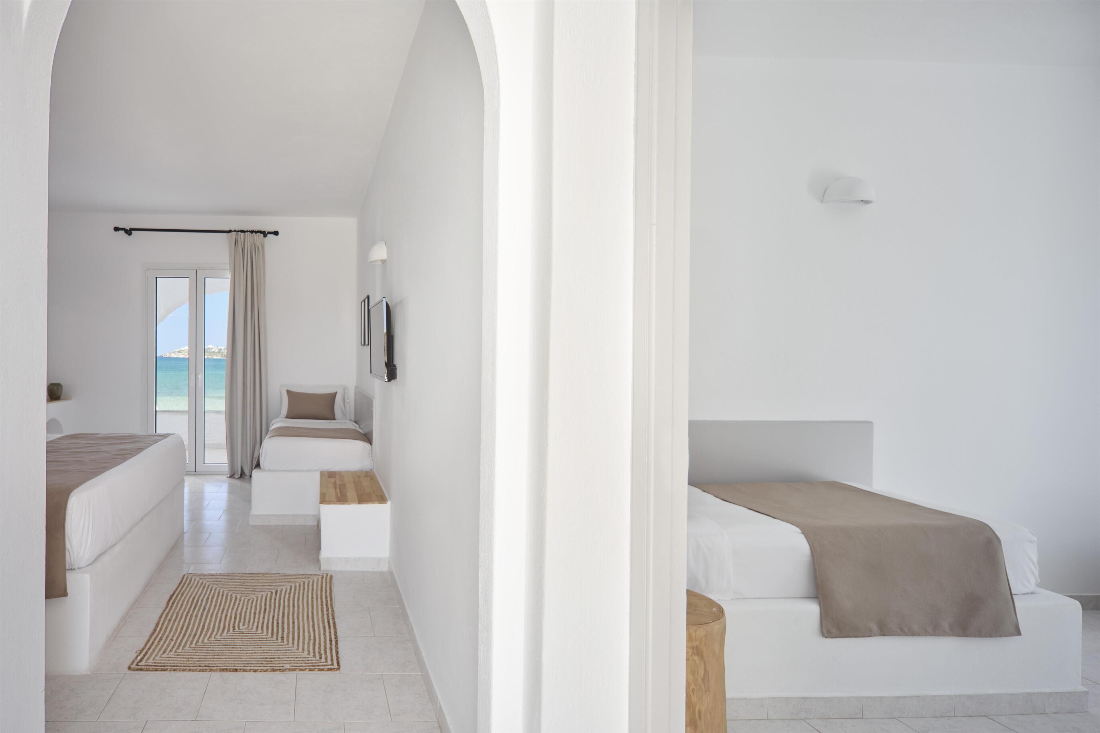 A modern hotel room with a large window, a bed, a bedside table, and a view of the sea.
