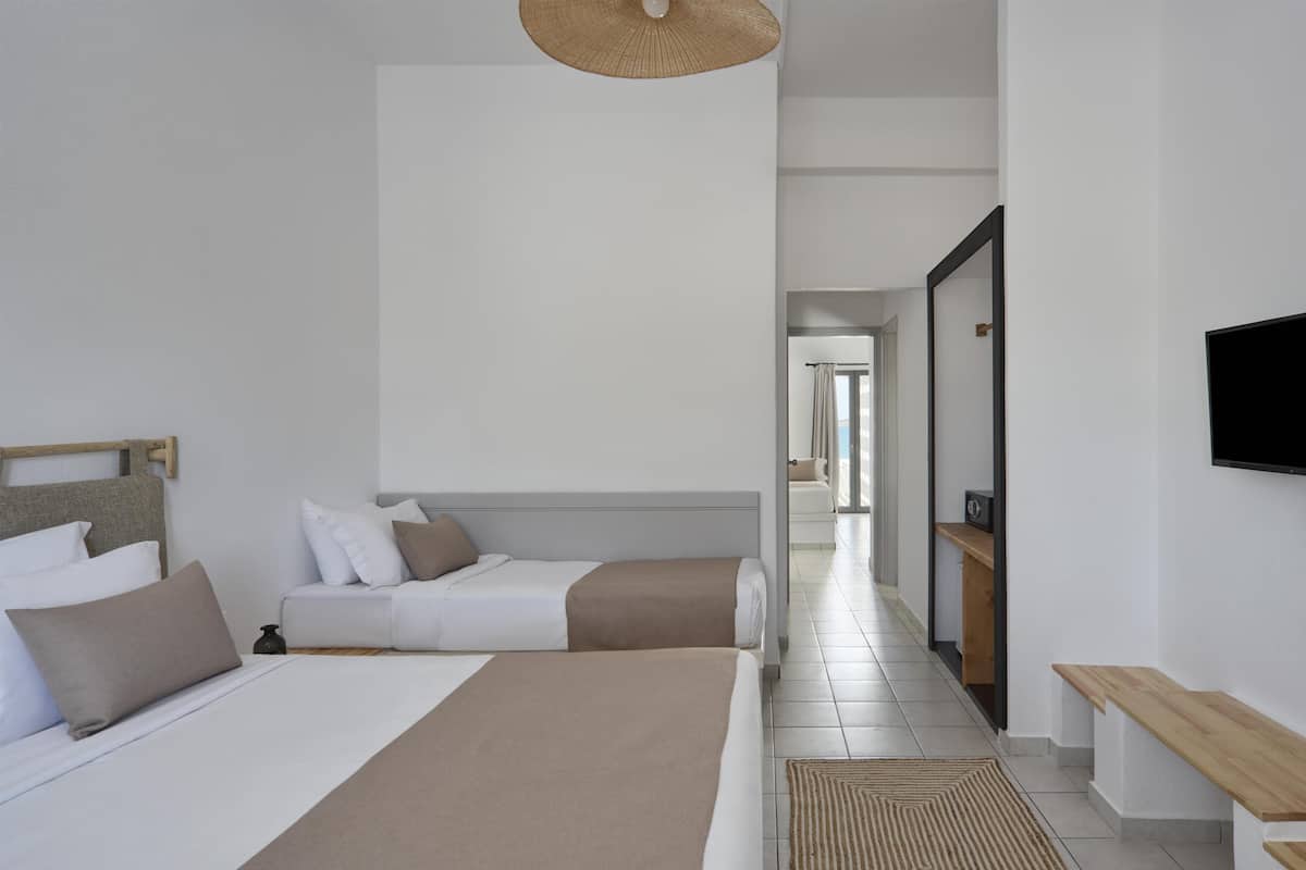 A modern hotel room with a large bed, a sofa, a TV, and a wooden bench.