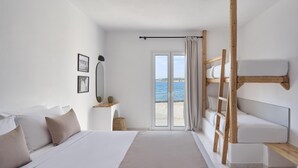A bedroom with a bed, a wooden ladder, a small table, and a view of the sea through a sliding door. - Pounda Resort Paros, a member of Radisson Individuals (Pounta)