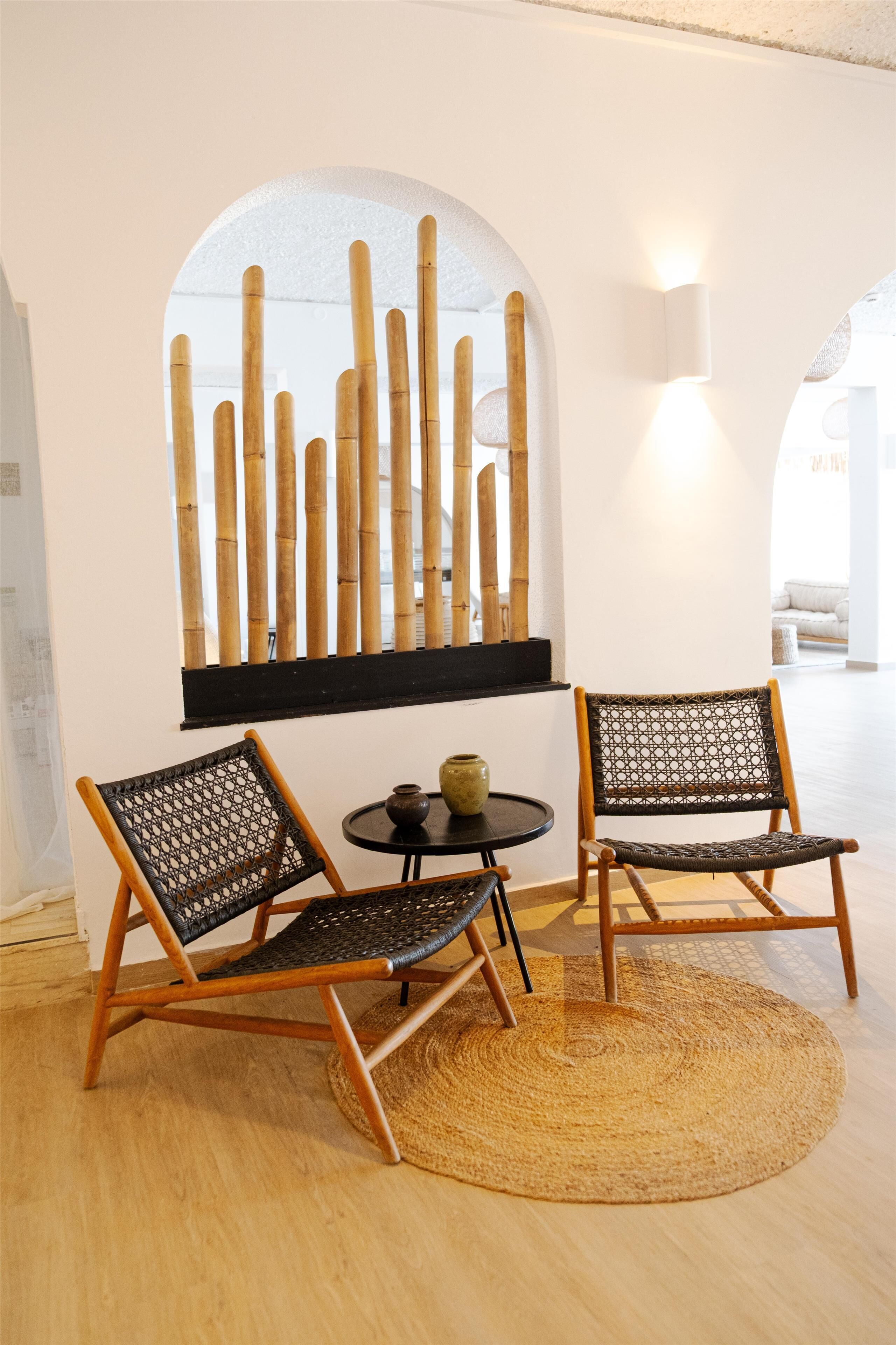 A room with two woven chairs, a small table with a vase, and a wall-mounted bamboo decoration.