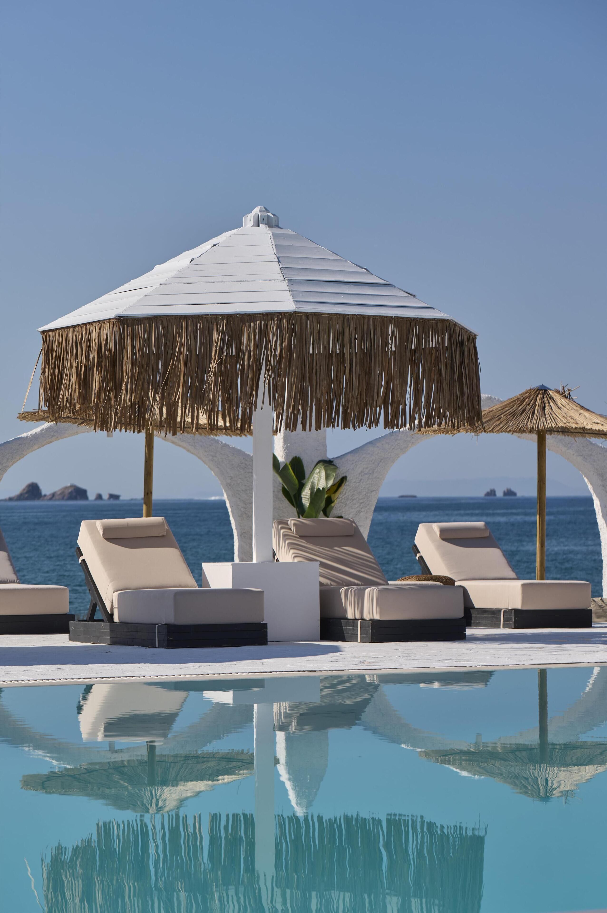 A poolside area with lounge chairs, a thatched umbrella, and a view of the sea.