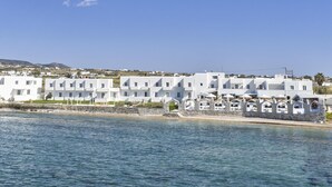 A coastal hotel with white buildings, a stone wall, and a clear blue sky. - Pounda Resort Paros, a member of Radisson Individuals (Pounta)