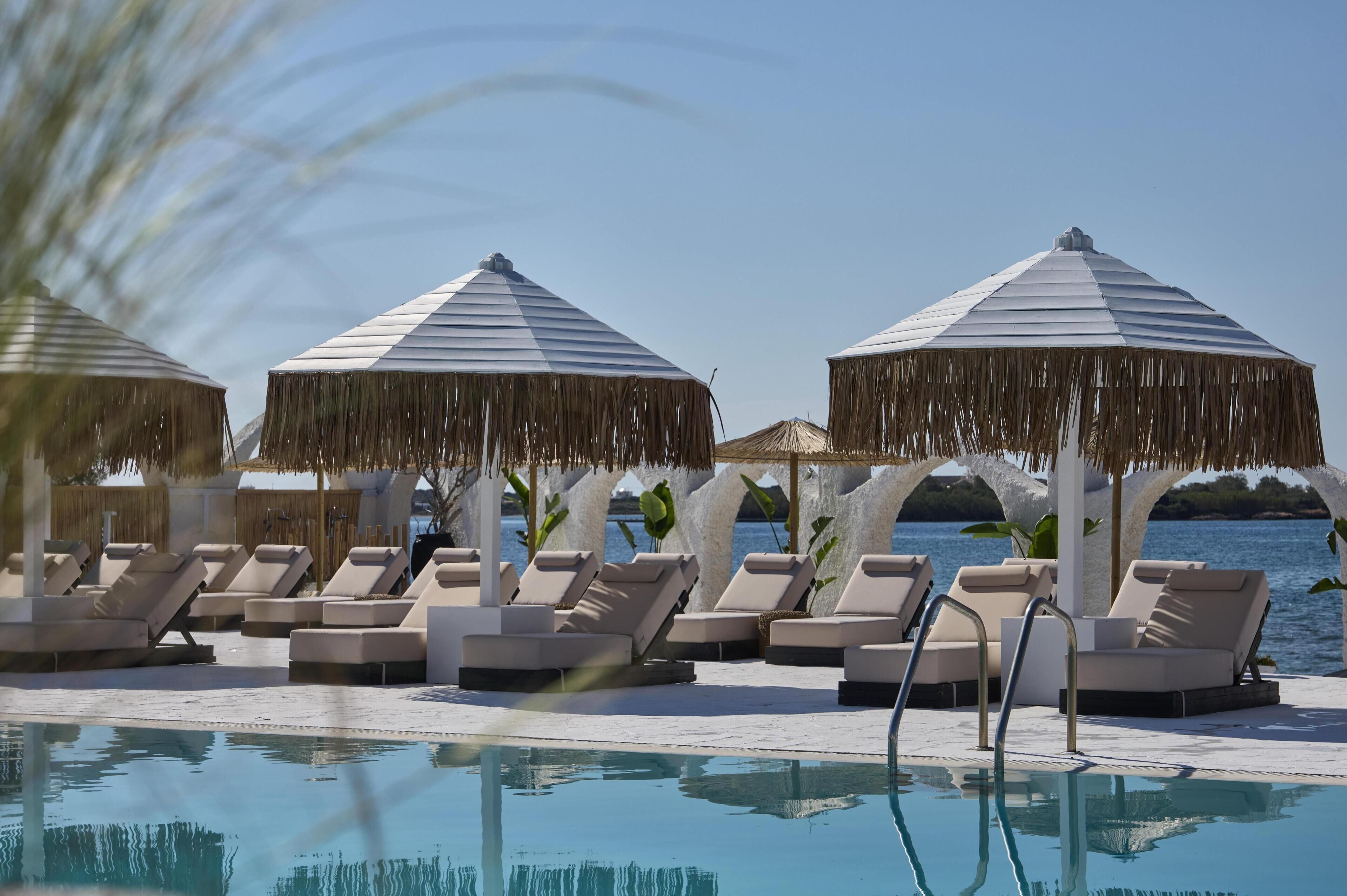 A poolside area with lounge chairs, umbrellas, and a view of the sea.