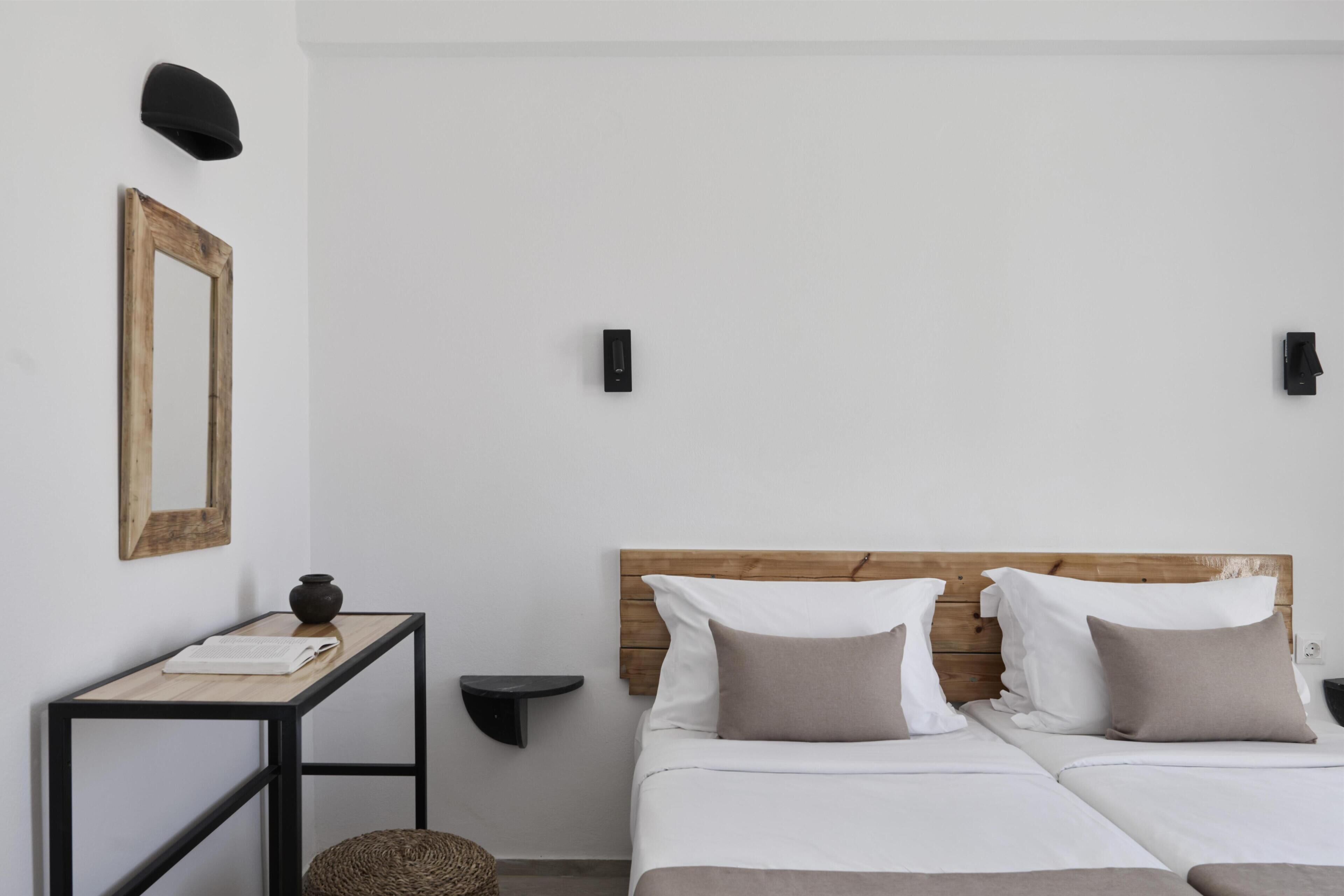 Un dormitorio con cabecera de madera, dos camas, una mesita de noche, un espejo e iluminación en la pared.