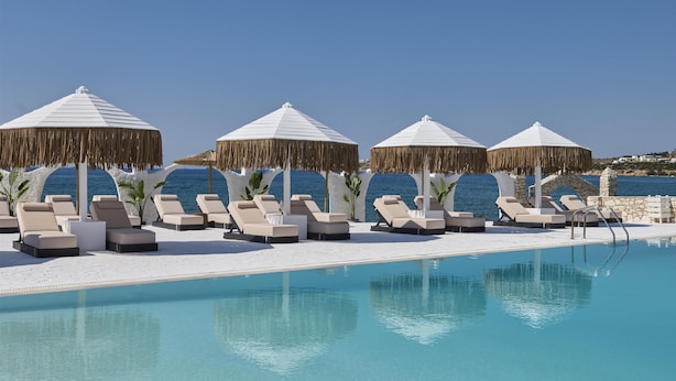A poolside area with lounge chairs and umbrellas, a clear blue sky, and a view of the sea. - Pounda Resort Paros, a member of Radisson Individuals (Pounta)