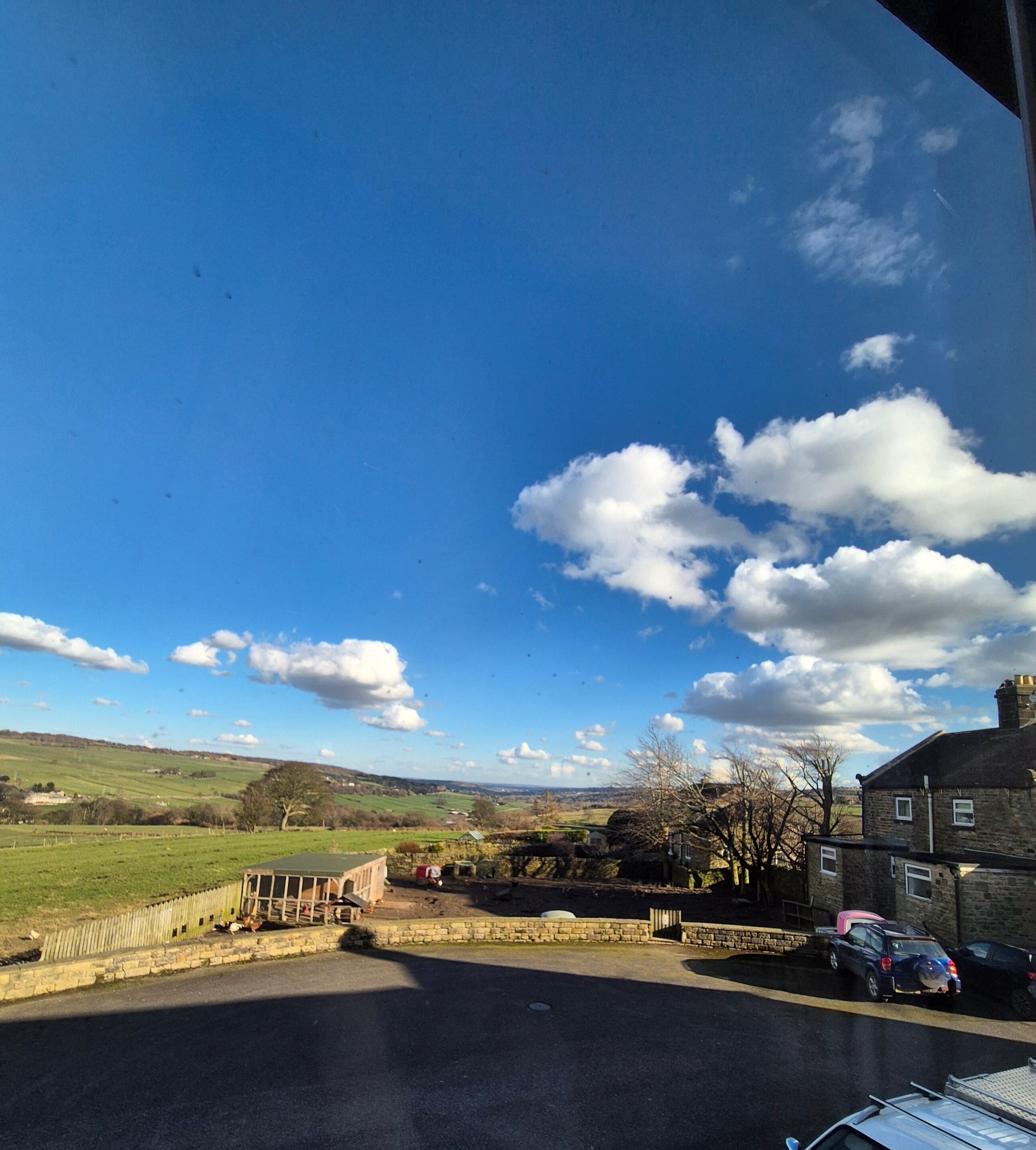 Ländliche Landschaft mit blauem Himmel, einer Steinmauer und geparkten Autos.