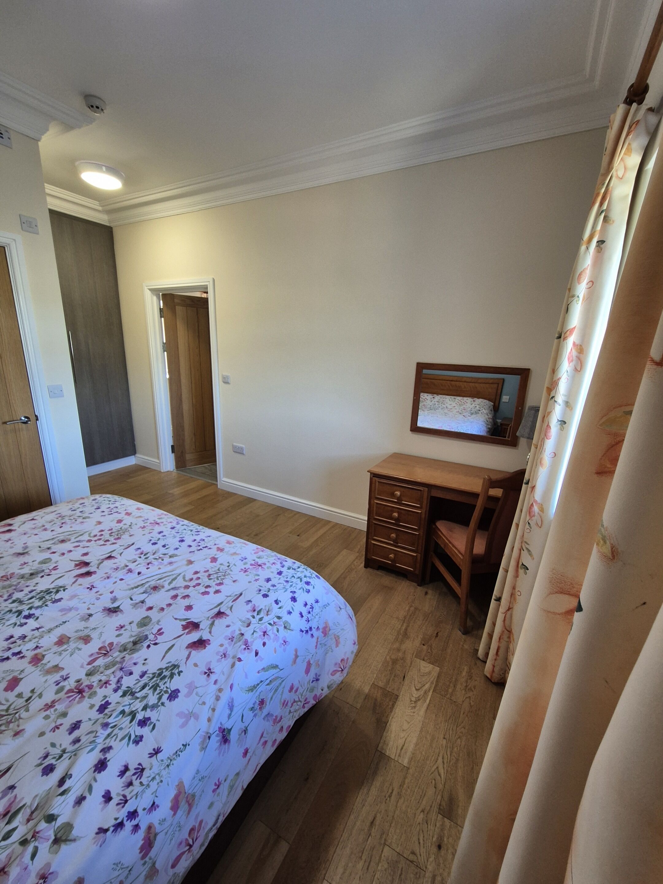 Ein Schlafzimmer mit einem Bett, einem Schreibtisch, einem Stuhl, einer Tür und einem an der Wand hängenden Bild.