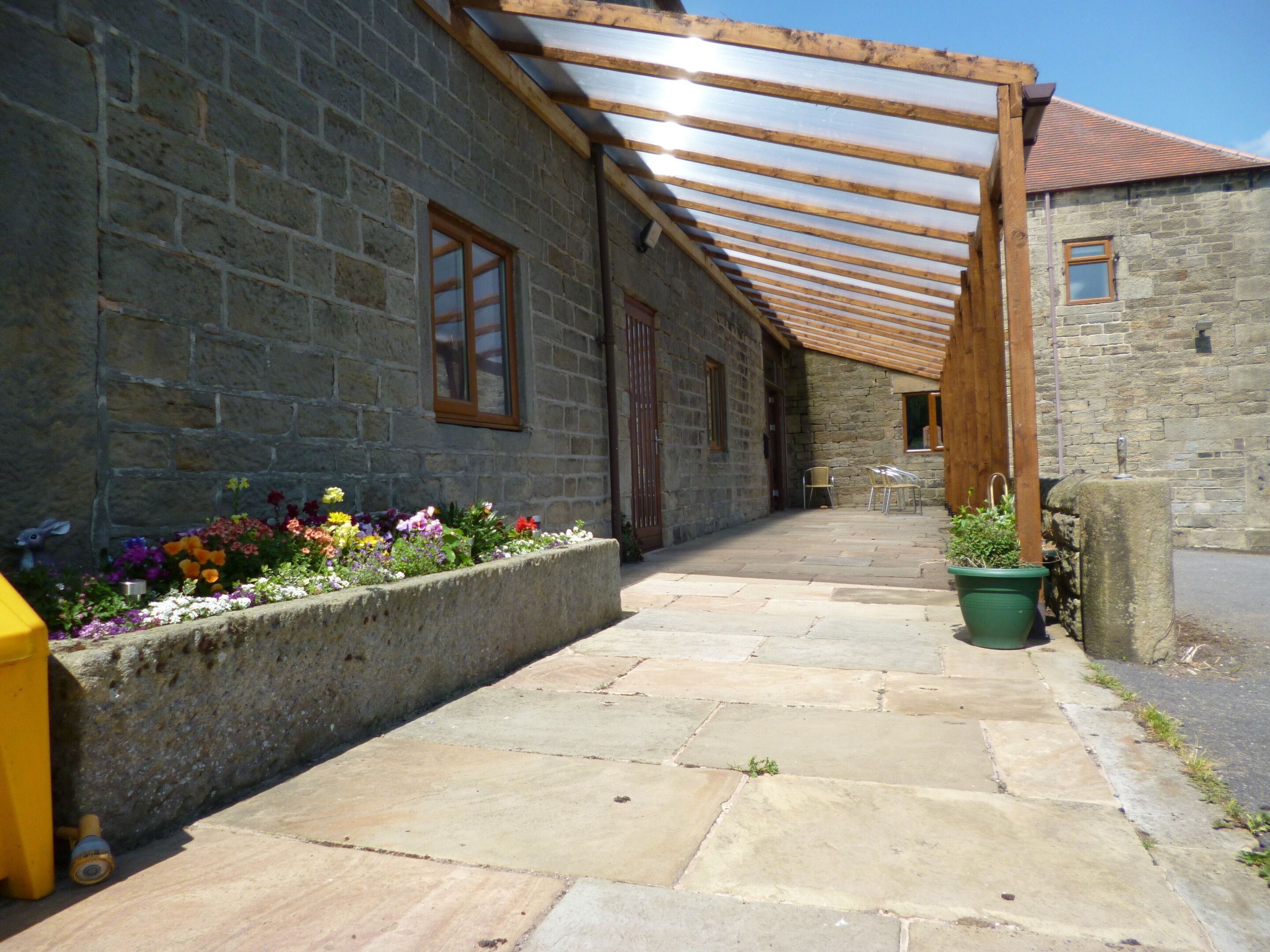 A stone building with a covered patio area, stone flooring, and a flower bed with various flowers.