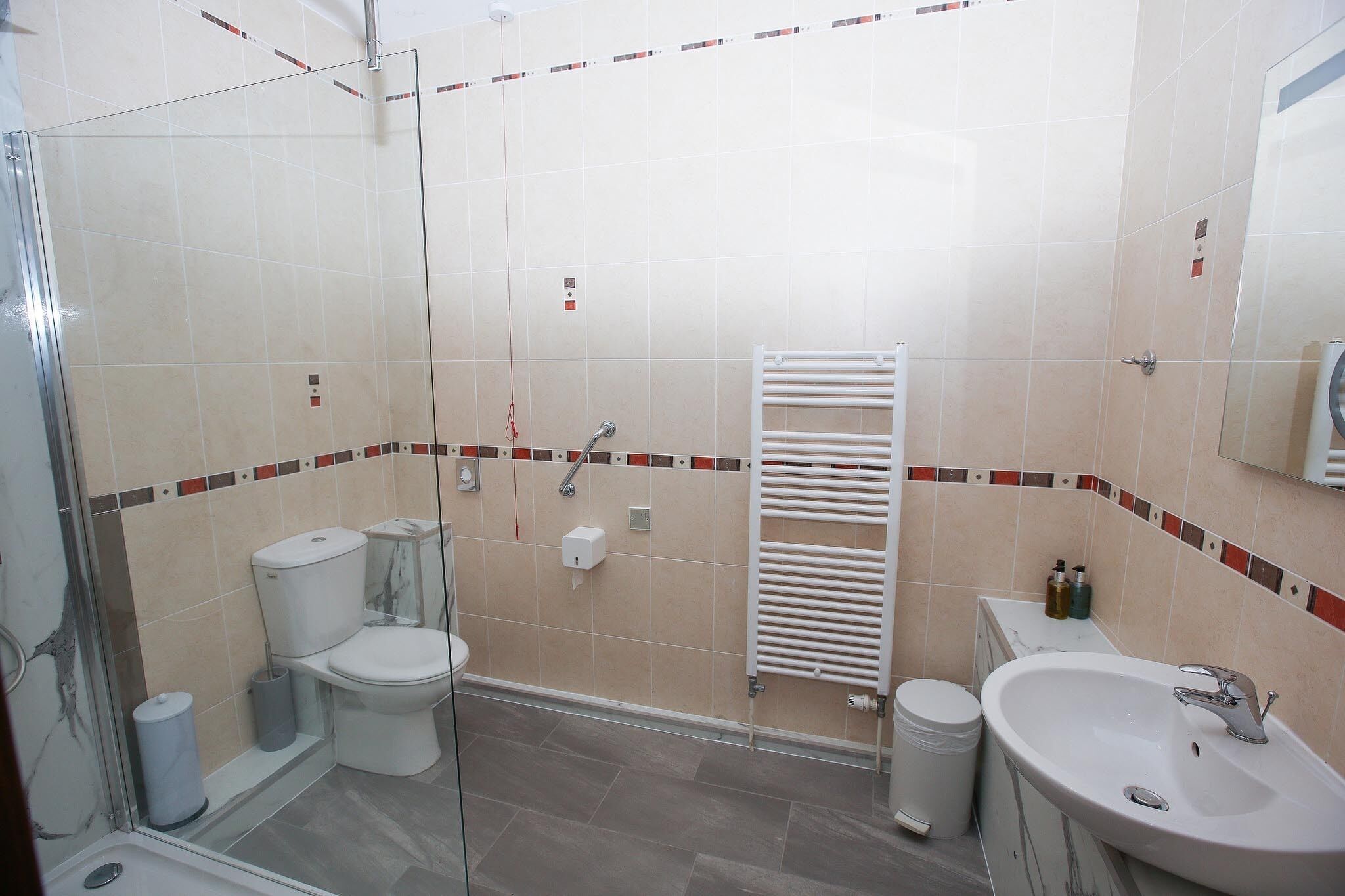 A bathroom with a glass shower enclosure, a toilet, a sink, and a towel rack.