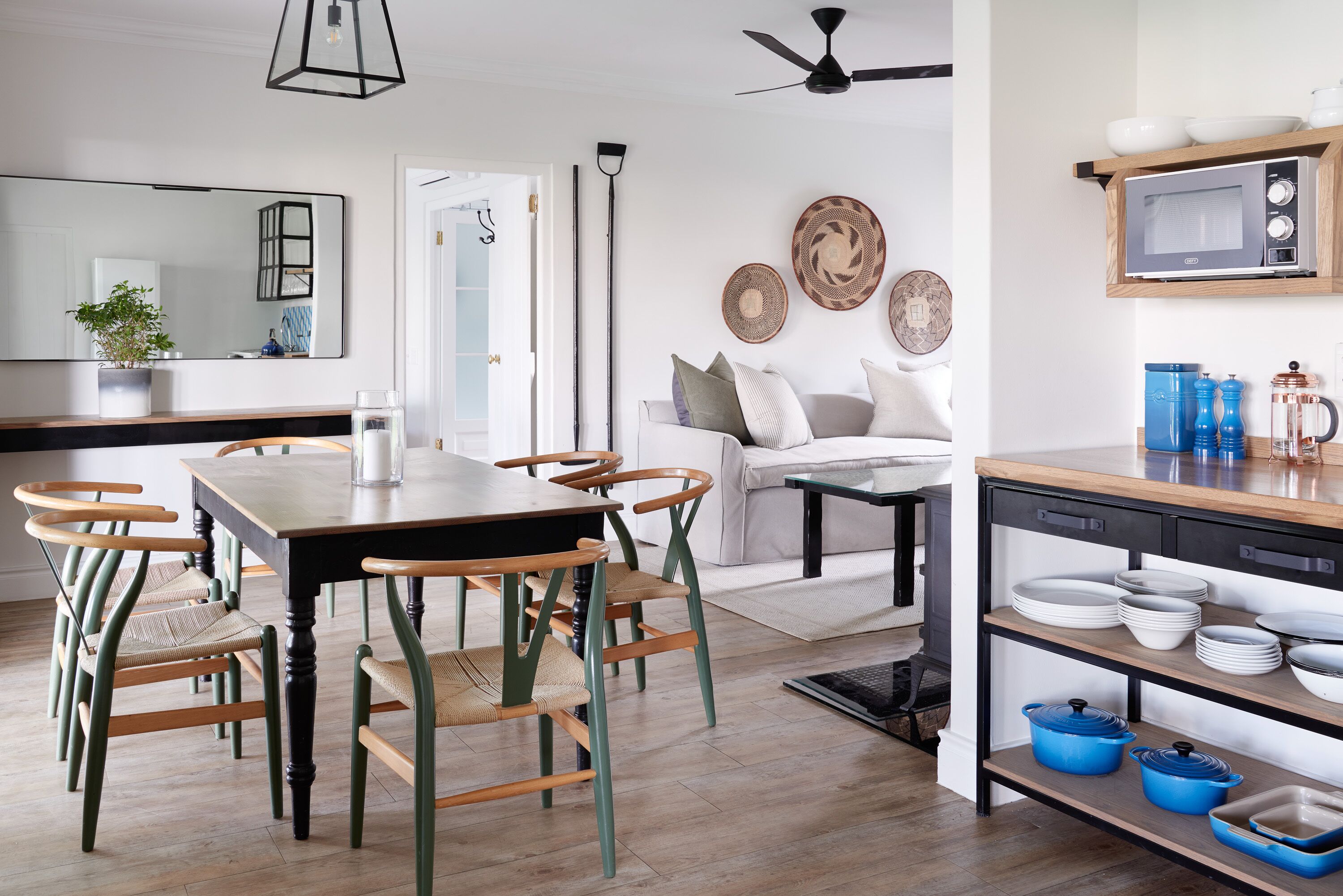 A modern kitchen with a dining area, wooden chairs, a white sofa, and a ceiling fan.