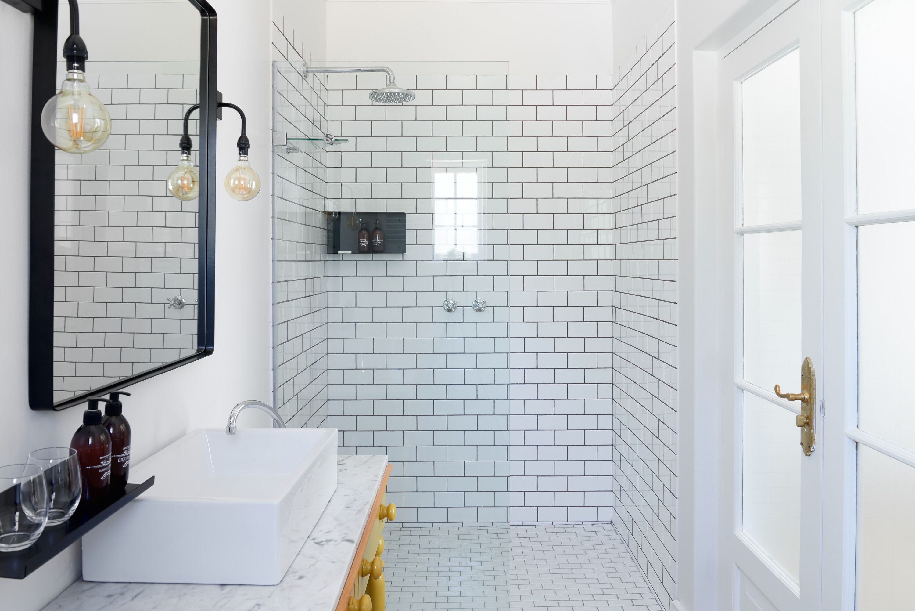 A modern bathroom with white subway tiles, a white sink, and a shower with a glass enclosure.