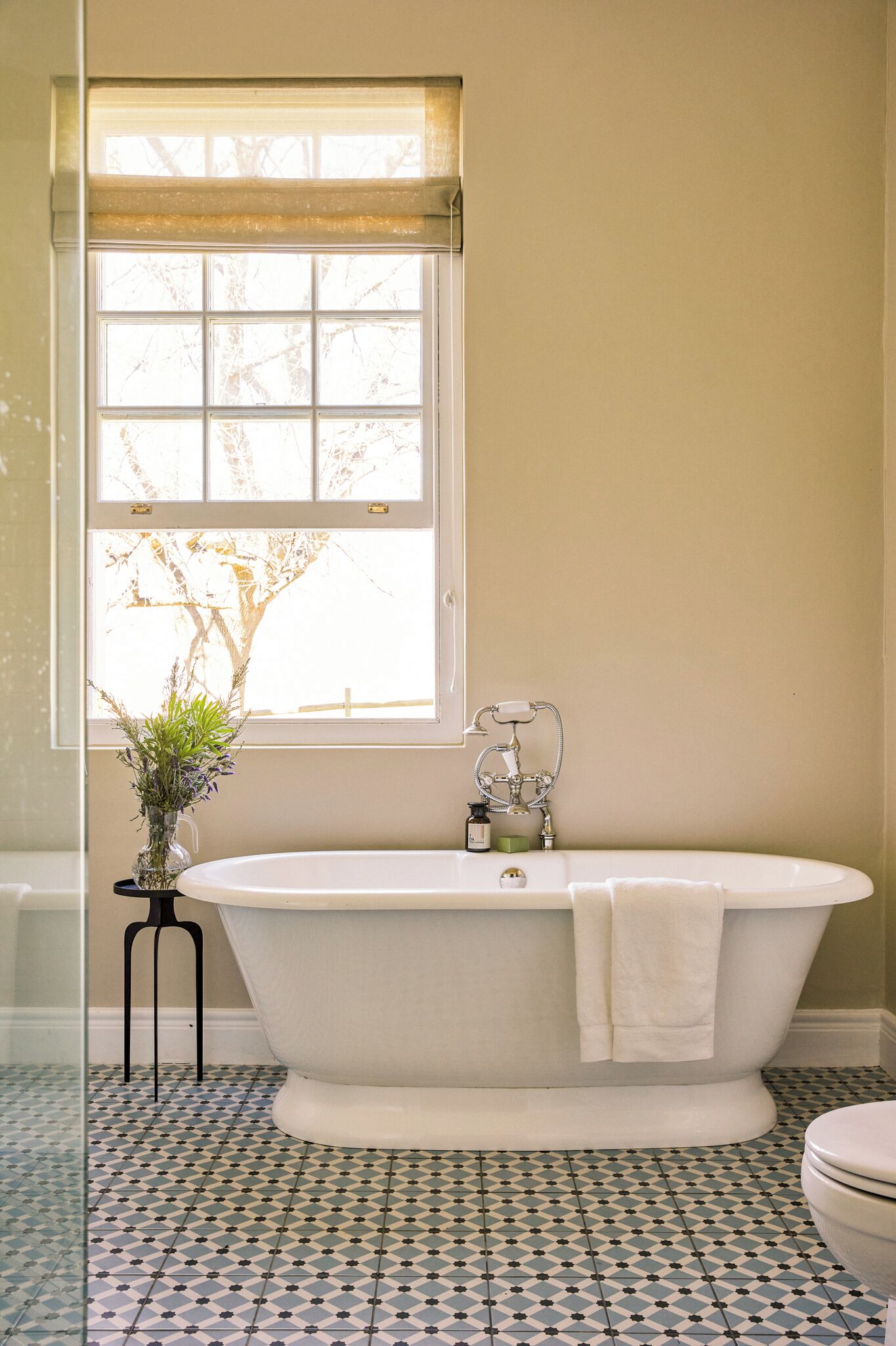 A bathroom with a freestanding bathtub, a window with a view of trees, and patterned floor tiles.
