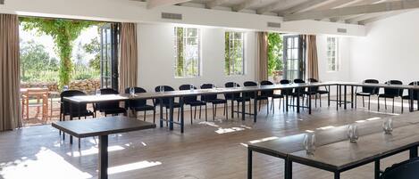 Une salle de conférence dotée de longues tables et de chaises, de grandes fenêtres et d’un plafond en bois.