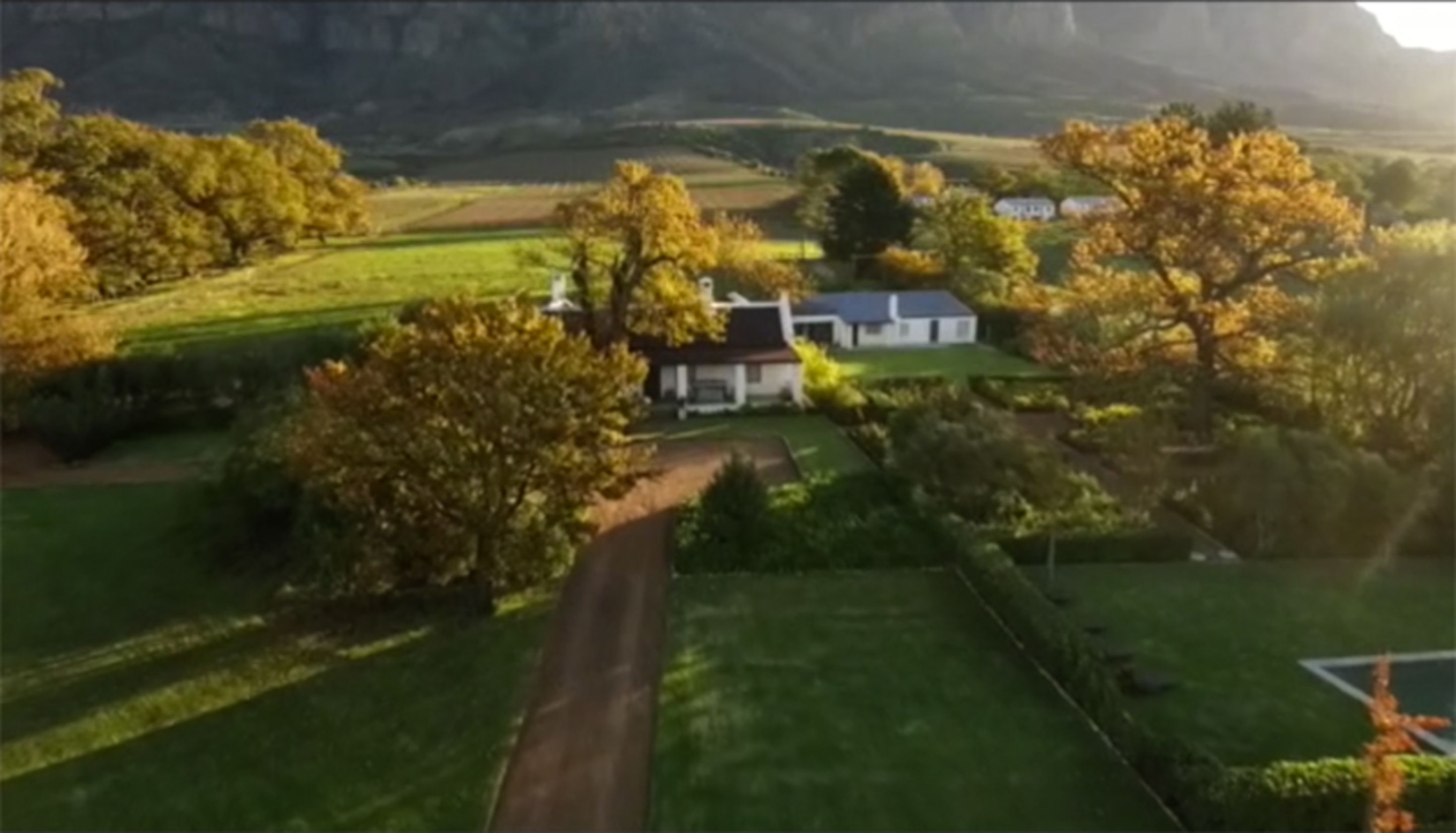 Vue aérienne d’une propriété rurale, avec une maison entourée de champs et d’arbres.