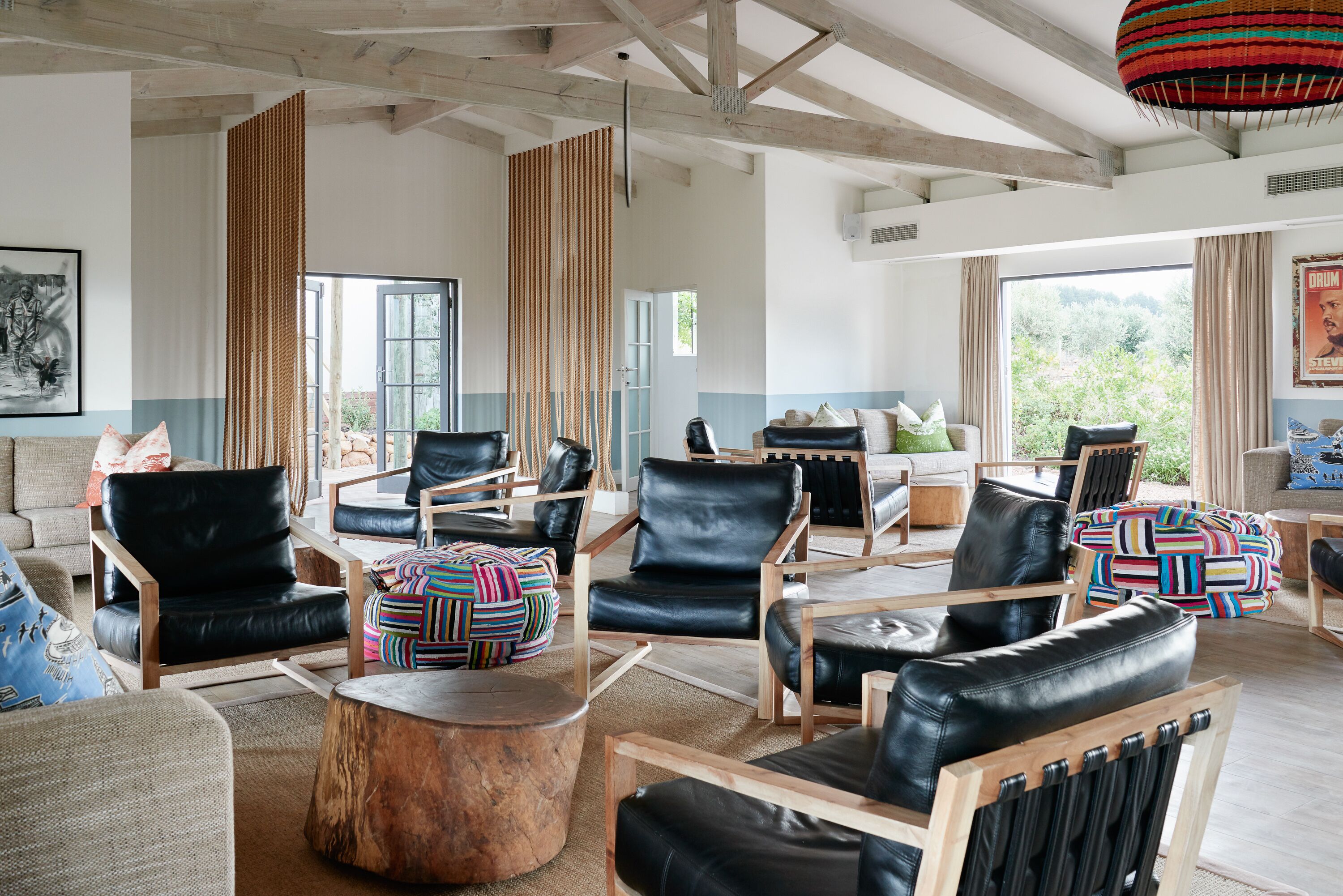 A spacious living area with multiple leather chairs and sofas, wooden accents, and large windows offering a view of greenery.