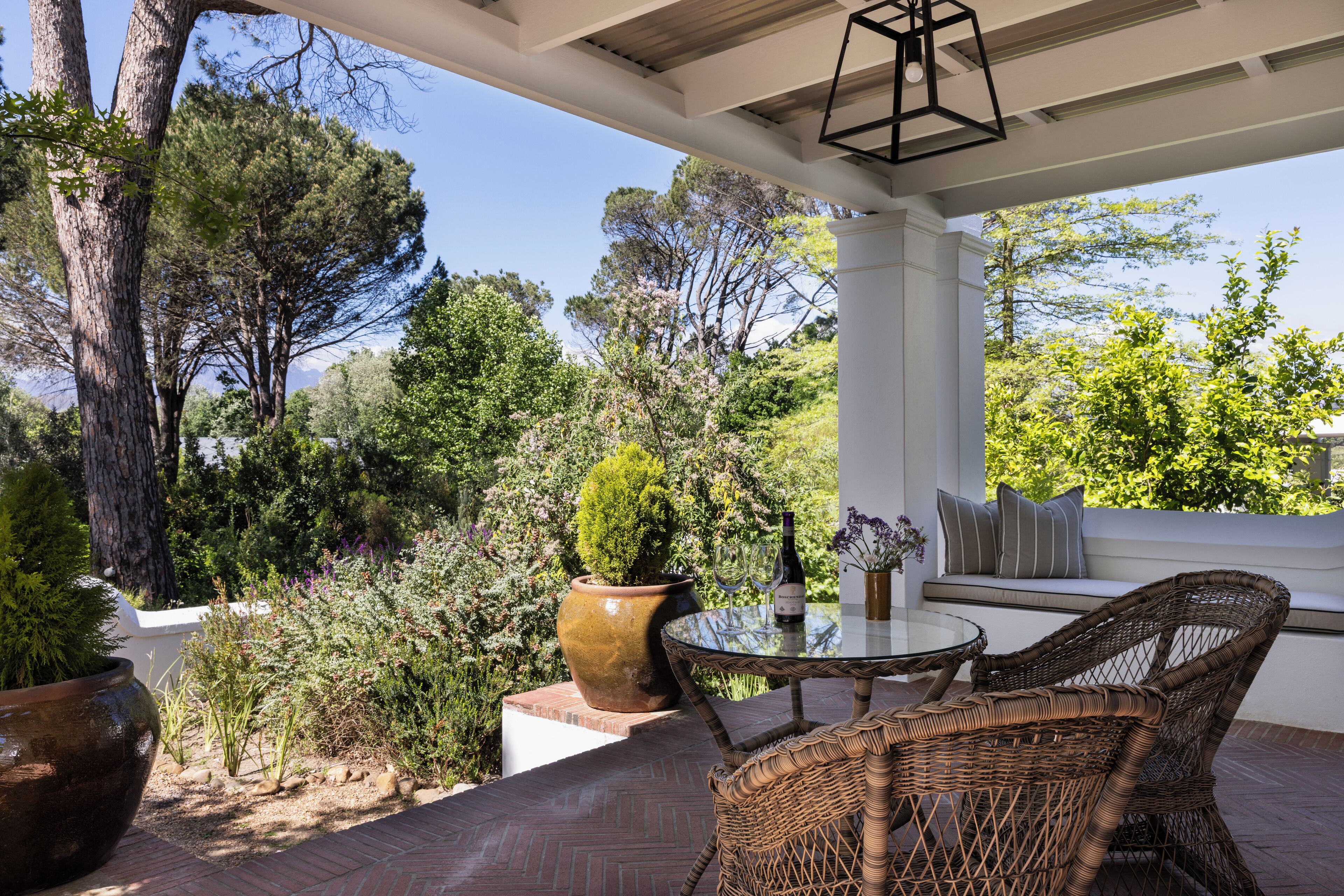 An outdoor patio with wicker furniture, a glass table, and a wine bottle.