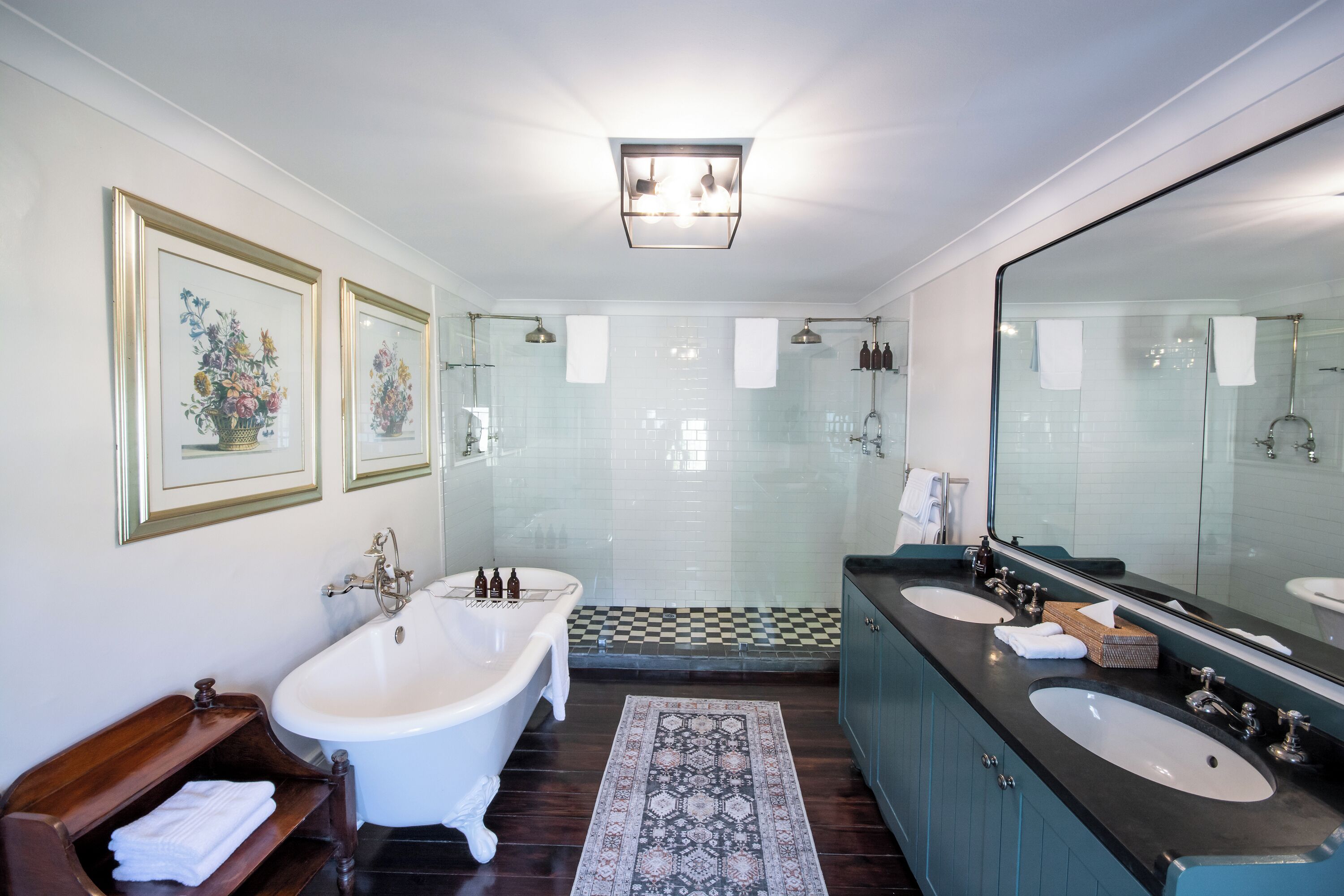 A modern bathroom with a freestanding bathtub, two sinks, a large mirror, and a patterned rug.